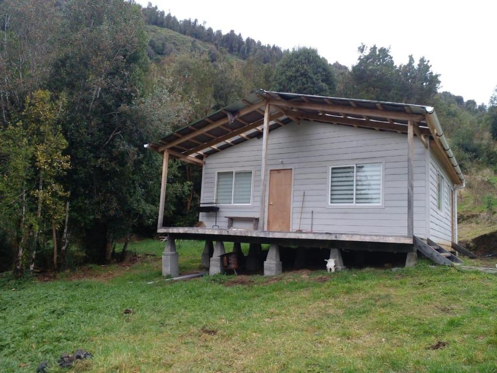 a house with a porch on top of a field at Cabañas Uenke in Puerto Puyuhuapi