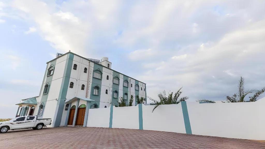 a white building with a car parked in front of it at Ras Al Hadd Guest House in Al Ḩadd