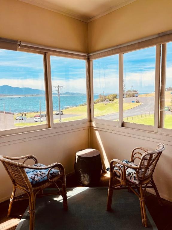 a room with two chairs and windows looking out at the ocean at Bermagui Bay Beach House 2, Wonderful Beachside Location, Pet Friendly in Bermagui