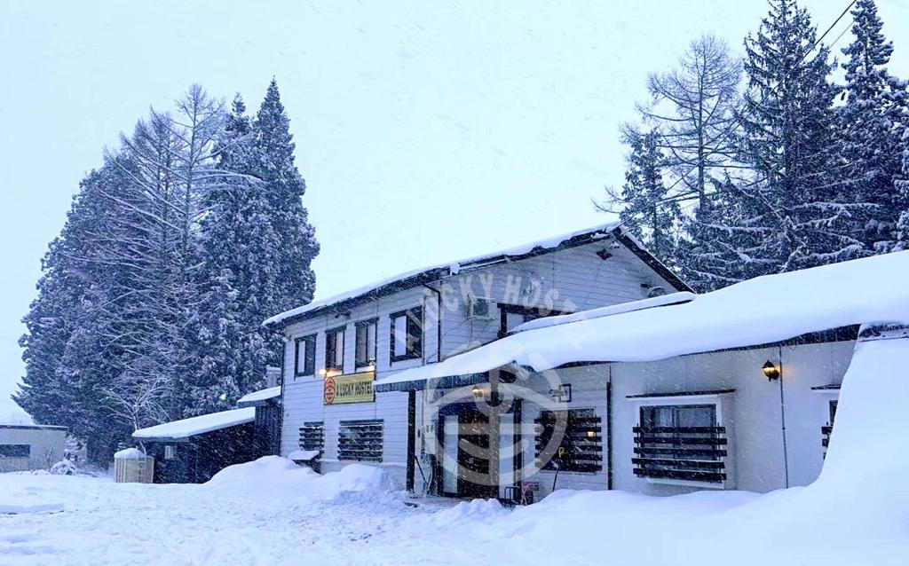 a building covered in snow with trees in the background at A Lucky Hostel in Hakuba