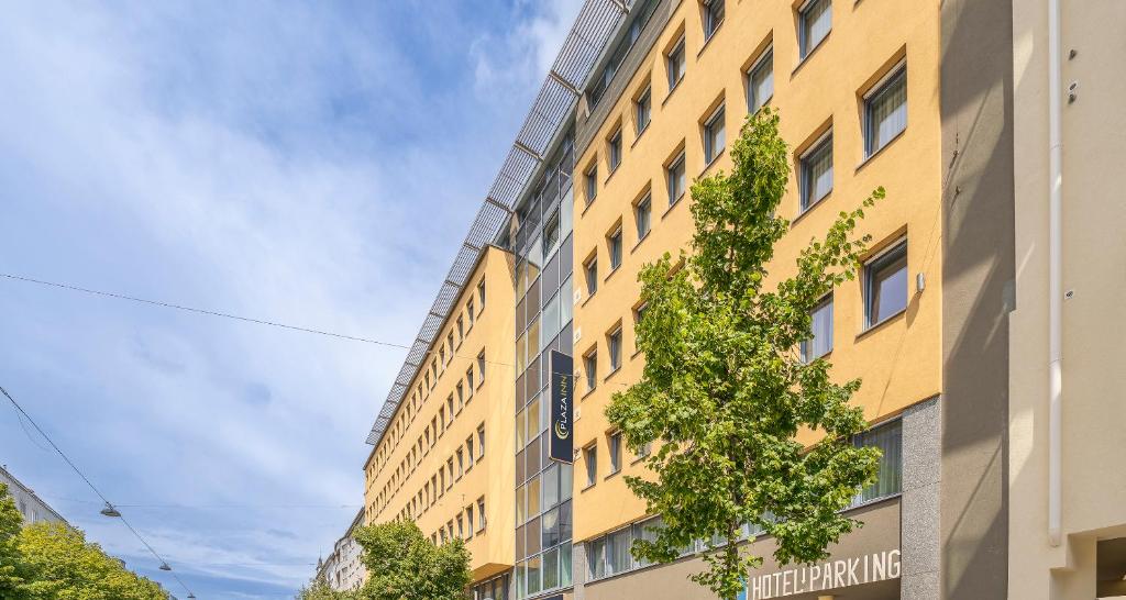 a yellow building with a tree in front of it at PLAZA INN Amedia Wien in Vienna