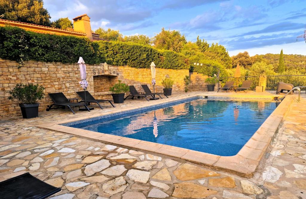 a swimming pool in a yard with chairs and a wall at Le Mas de San Lou in Cabasse