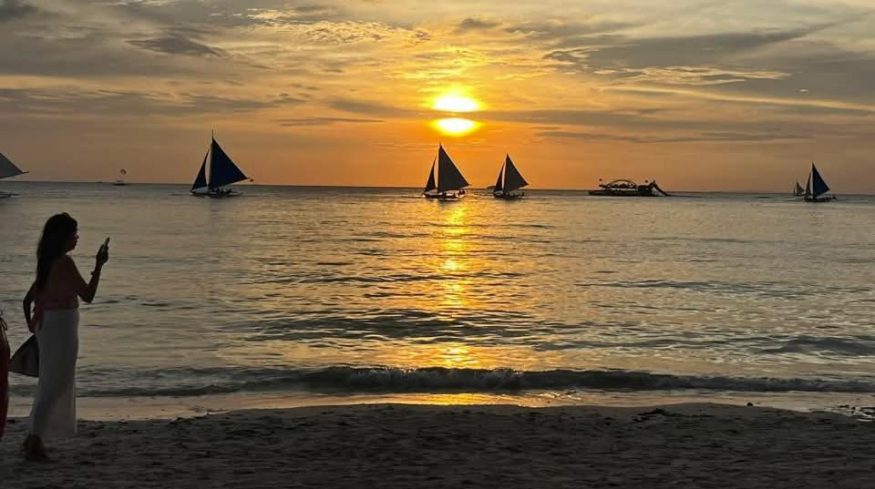 a woman standing on the beach at sunset with sailboats at Sla guest house in Boracay