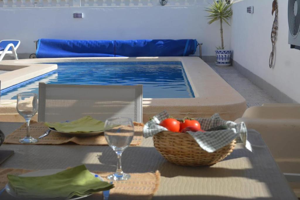 a table with a basket of fruit and wine glasses next to a swimming pool at SUPERBE MAISON VISTABELLA Golf in Orihuela Costa