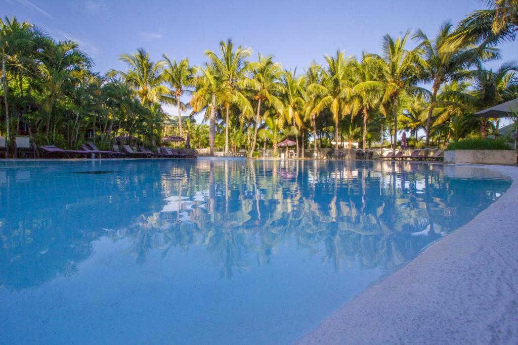 a swimming pool with palm trees and blue water at Hotel Exsel Floralys in Étang-Salé les Bains