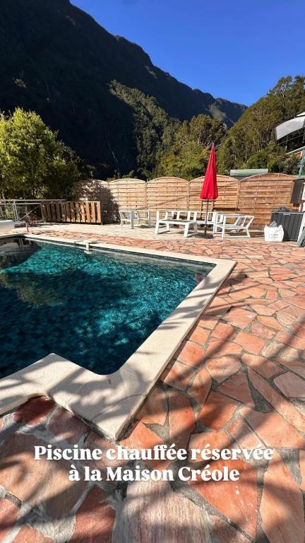 a swimming pool with a table and a red umbrella at Le Voile de la Mariée in Salazie