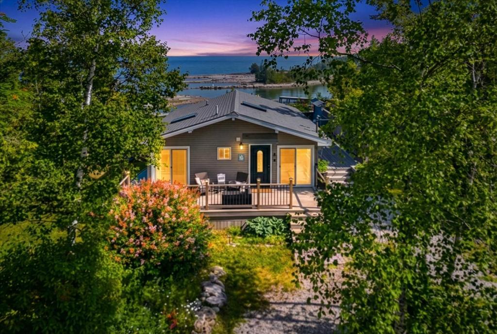 a house with a porch and a deck with chairs at Sunset Cove AC Waterfront Kayaks in Tobermory