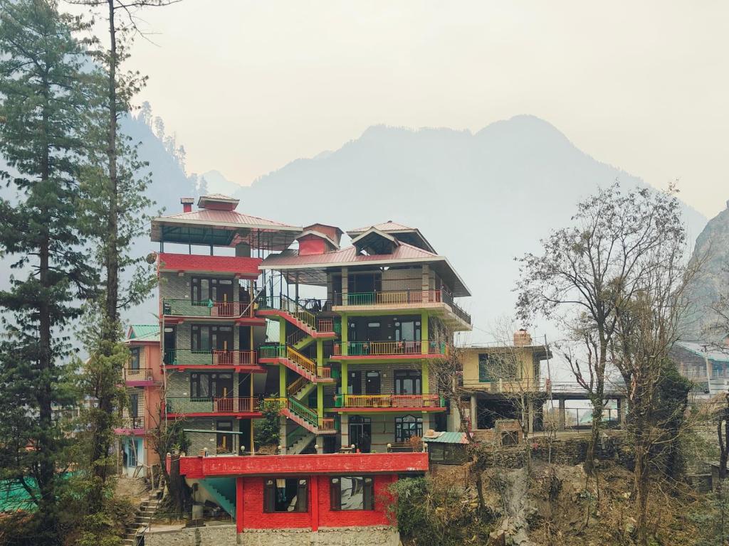 a building on a hill with trees and mountains at Parbati Headquarters in Kasol