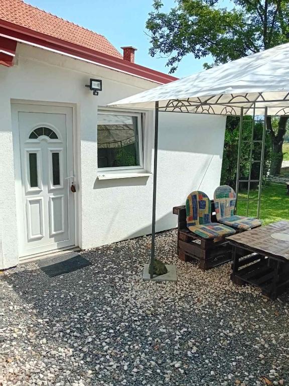 una casa bianca con tavolo e sedie sotto un ombrellone di Ravne Apartman a Visoko