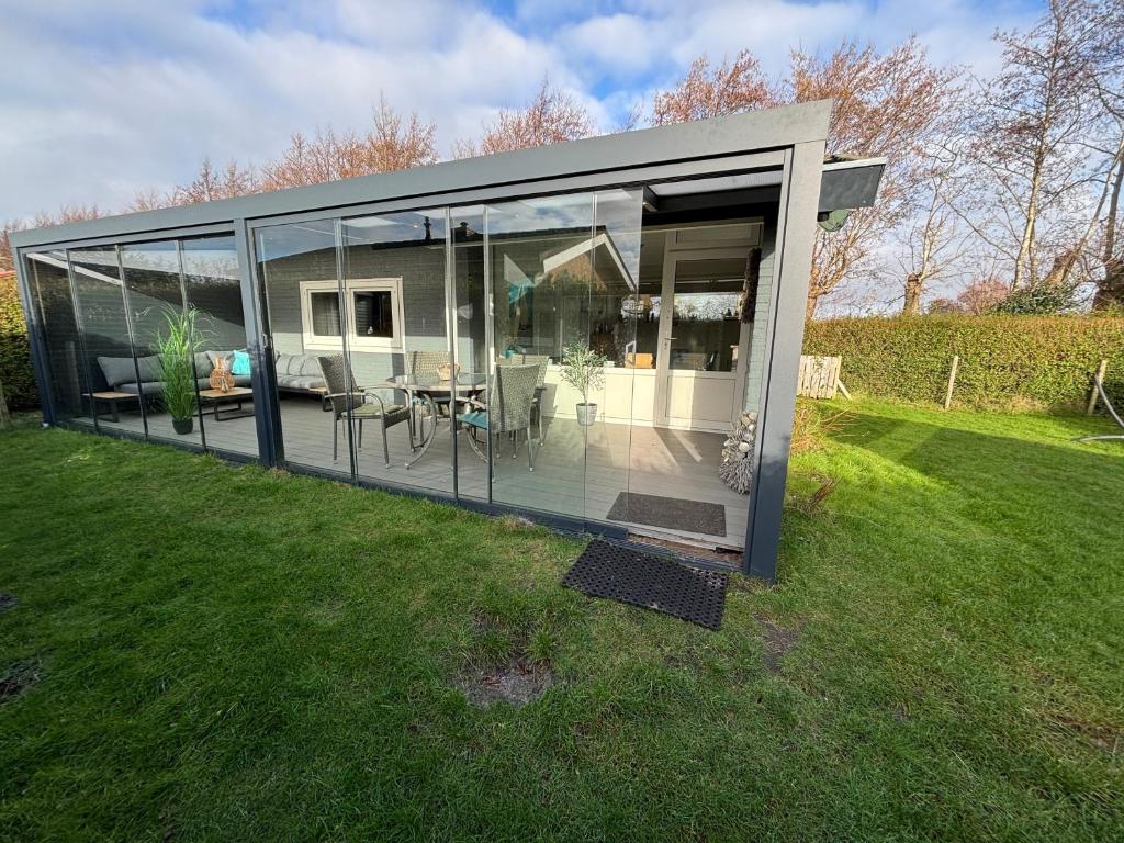 a glass house with a table and chairs in a field at Strandnahes Ferienhaus NR 2 mit Wintergarten grosser uneinsehbarer Garten in Sint Maartensvlotbrug