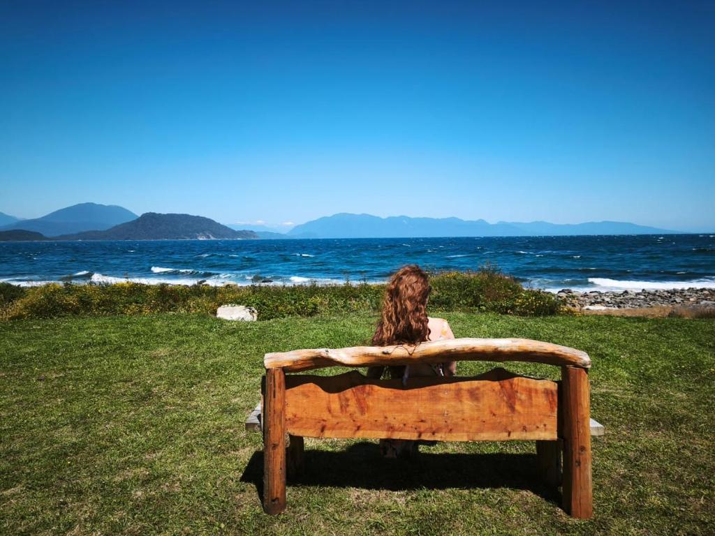 a woman sitting on a bench looking at the ocean at CABAÑA HUALAIHUE AUSTRAL in Hornopiren