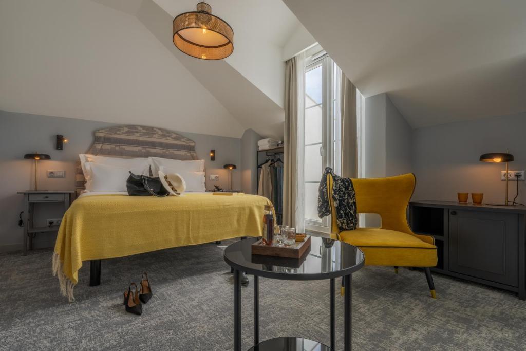 A spacious attic bedroom with a yellow armchair, a second seat and a narrow central window.