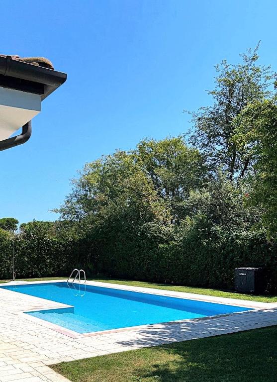 a blue swimming pool with trees in the background at Albarella Family Villa with Private Pool and Garden in Isola Albarella