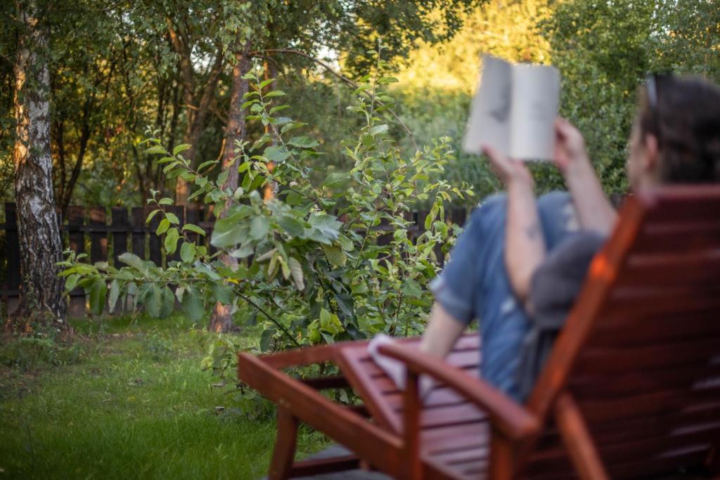 a woman sitting on a bench reading a book at Lawendowe Pole - Domek Różany in Nowe Kawkowo