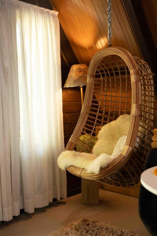a hanging rattan chair in a room with a window at Recanto do Rio Chalé na Natureza in Rio dos Cedros