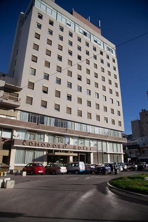 a large white building with cars parked in front of it at Comodoro Hotel in Comodoro Rivadavia