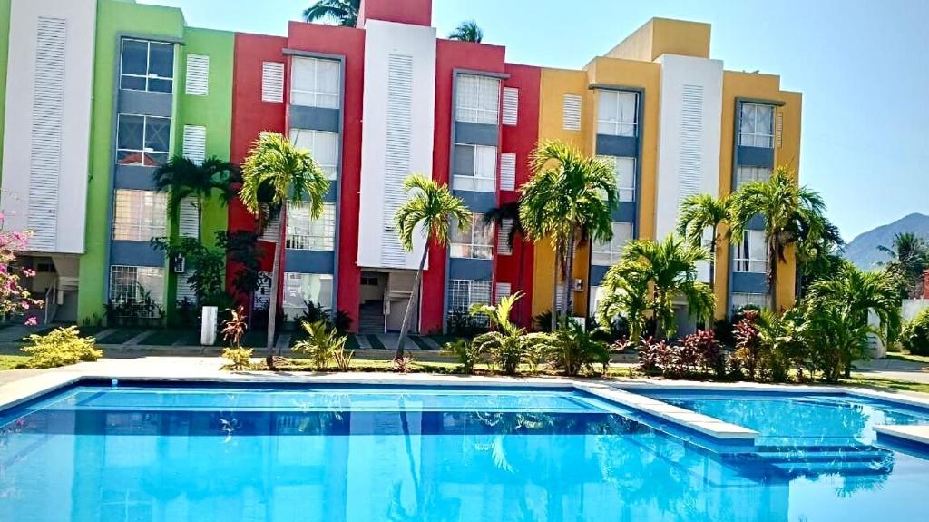 a pool in front of a building with palm trees at Acapulco Vibes - Departamento con Alberca Cerca de Punta Diamante in Acapulco