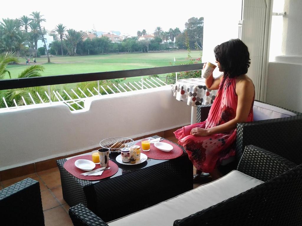 a woman sitting on a balcony talking on a cell phone at Casas Nuestras Andalucia Roquetas de Mar- Amazing terrace with view , 2 outdoor swimming pools , free wifi and parking in Roquetas de Mar