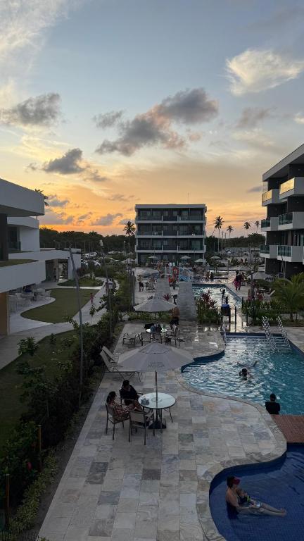 a resort with a pool and people sitting around tables at Flat Inteiro no Makia Beach Experience in Porto De Galinhas