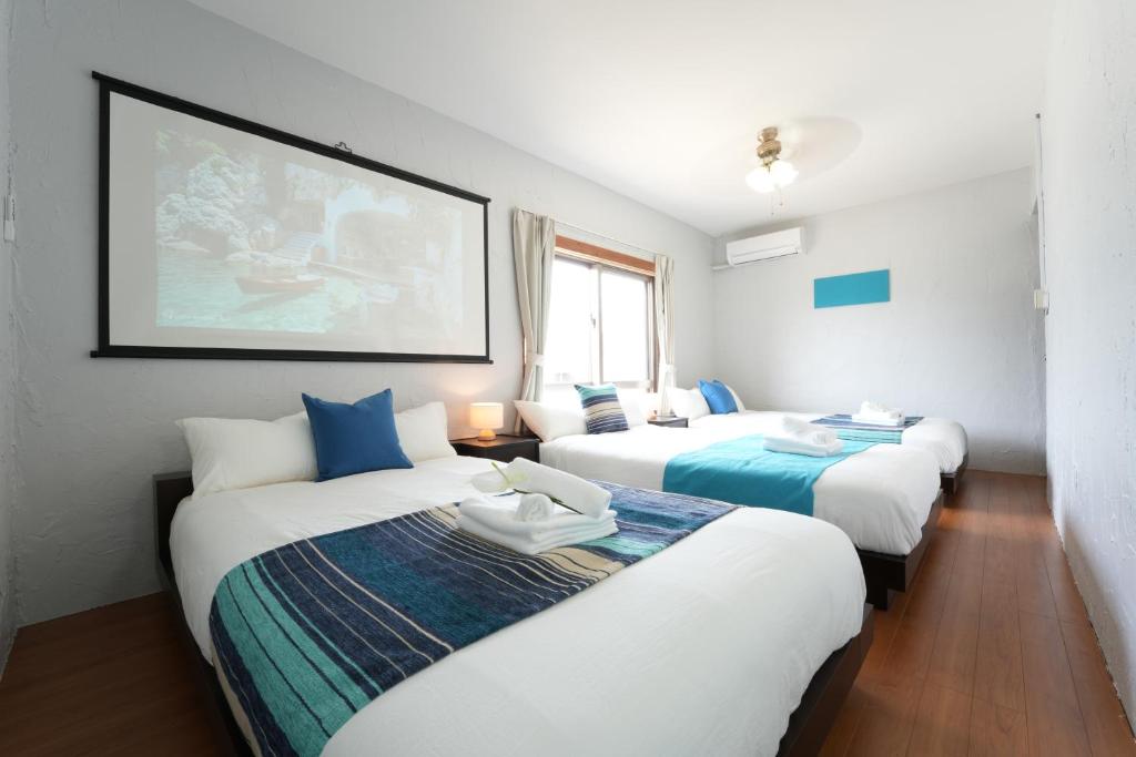 a hotel room with three beds and a picture on the wall at Retreat Ginoza in Ginoza