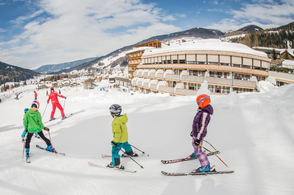 un gruppo di persone che sciano sulla neve di fronte a un rifugio da sci di Family Resort Rainer a Sesto