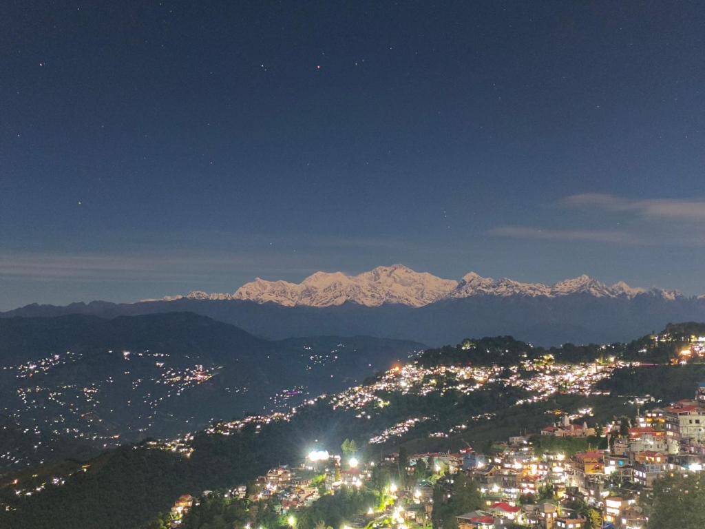 a view of a city at night with snow capped mountains at Tholangi Homes in Darjeeling