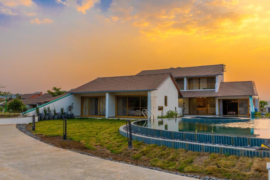 a house with a swimming pool in front of a sunset at Touchwood Bliss Nature Retreat - Igatpuri in Igatpuri
