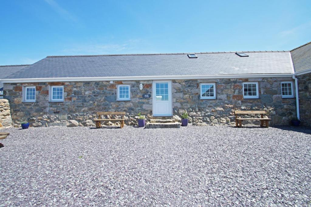 a stone house with two benches in front of it at Beudy Lleuddad in Llangwnadl