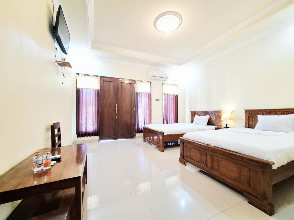 a bedroom with two beds and a table and a desk at Hotel Syariah Milik Kita Borobudur Mitra RedDoorz in Borobudur