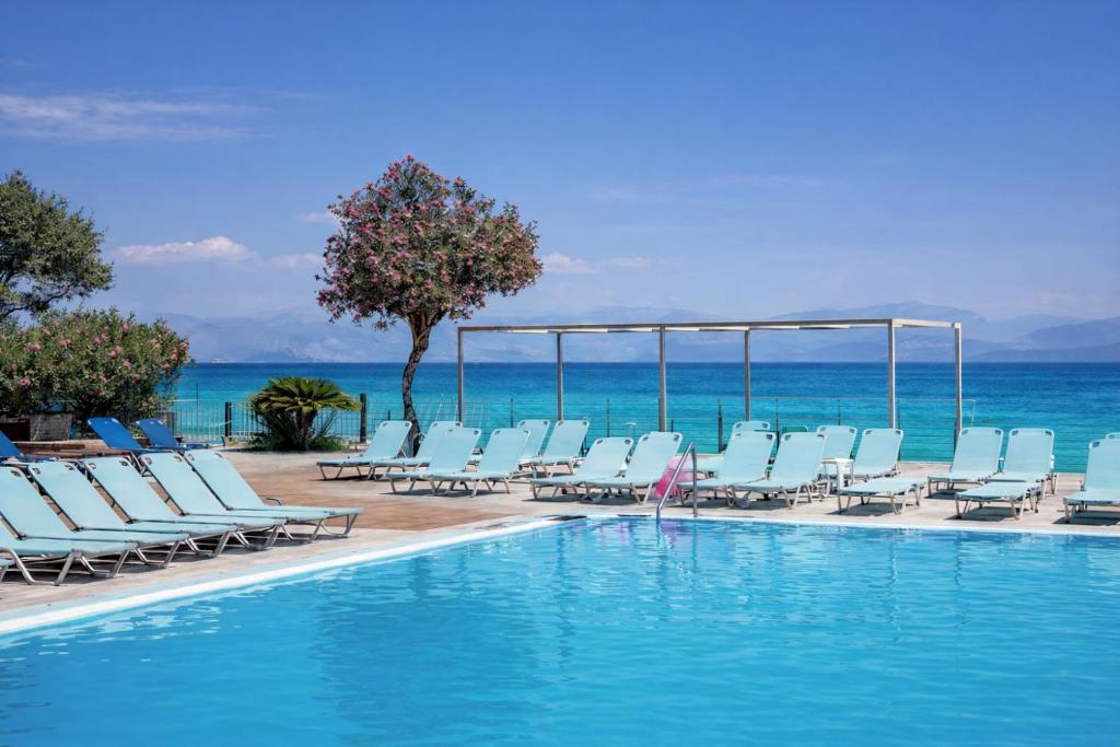 basen z krzesłami i oceanem w tle w obiekcie Agnes Beach Hotel Apartments w mieście Kavos