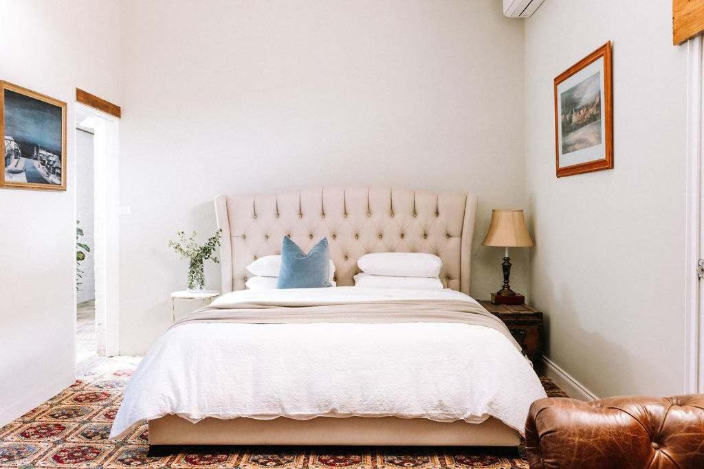 a white bedroom with a large bed with blue pillows at Miss Lucy Historic & Central in Beechworth