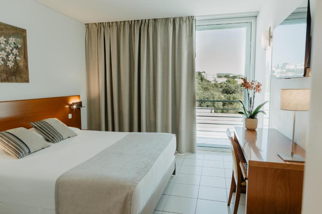 a hotel room with a bed and a desk and a window at Hotel Sao Sebastiao de Boliqueime in Boliqueime