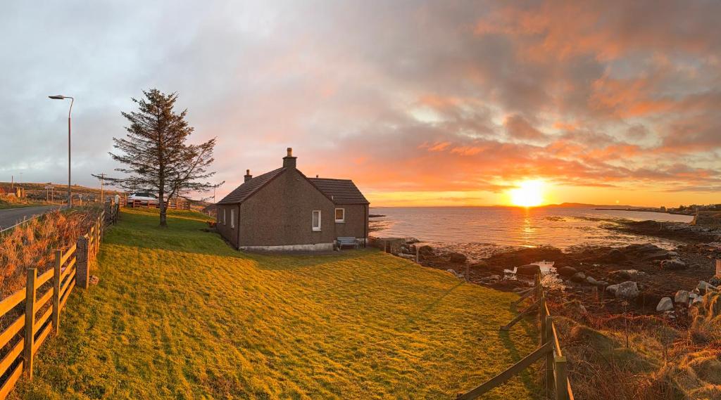 a house on the shore of the ocean at sunset at Berneray Otter Cottage in Berneray