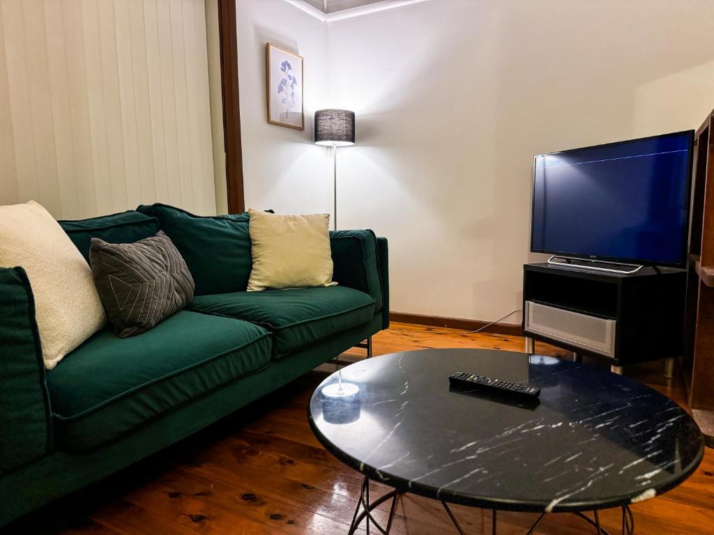 a living room with a green couch and a tv at Old Charm Guesthouse in Bass Hill