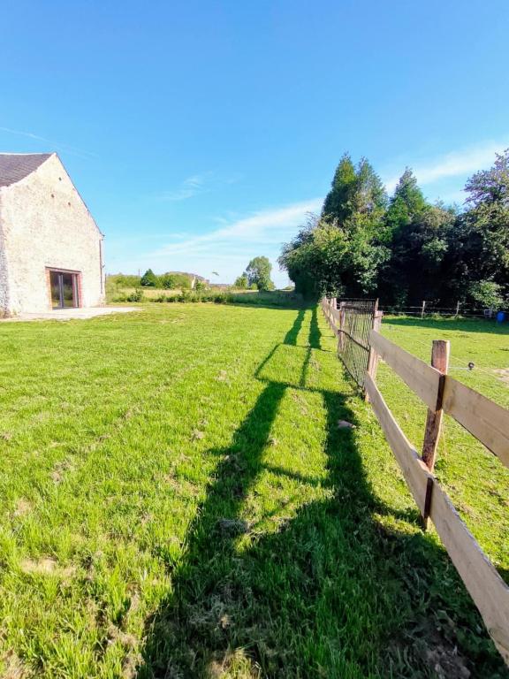 a fence in a field next to a barn at Grand gîte champêtre ! LA SOURCE DE NOS RACINES - CORPS DE FERME AU COEUR DU PARC NATUREL DE L'AVESNOIS in Beaufort