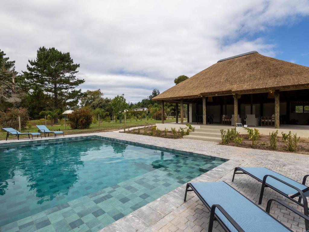 a swimming pool with chairs and a building at Five Elements Resort - Nguni Cabin in Harkerville