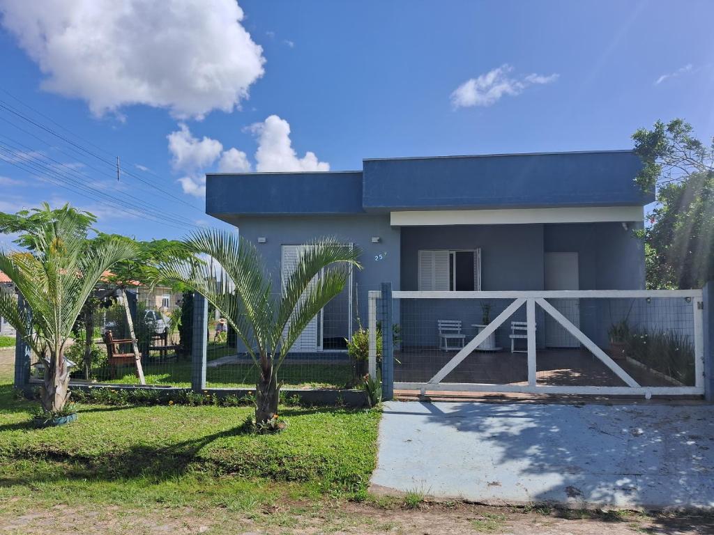 a house with a fence and palm trees in front of it at Casa Lovato in Arroio do Sal
