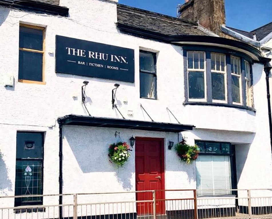 a white building with a red door and a sign on it at The Rhu Inn in Rhu