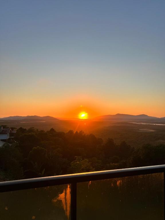 a sunset from a balcony with the sun setting at Chalé Sol Nascente - Vista espetacular próximo as melhores praias de Floripa in Florianópolis