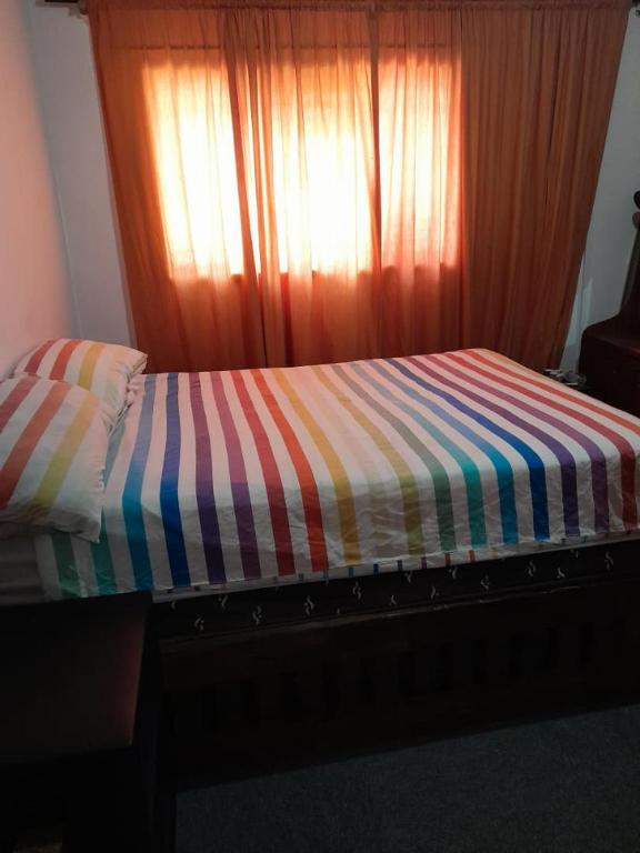 a bed with a striped comforter in front of a window at Dudes guesthouse in Francistown