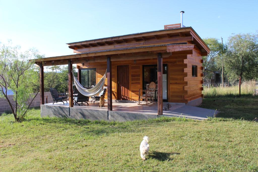 a small log cabin with a cat standing in the grass at Los Grillos Cabañas Serranas in Los Reartes