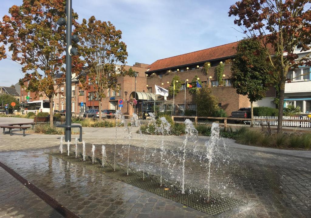 une fontaine au milieu d'une rue avec un bâtiment dans l'établissement De Basiliek, à Edegem