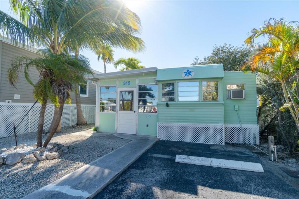 a green house with a palm tree in front of it at Cozy Conch Cottage in Cudjoe Key