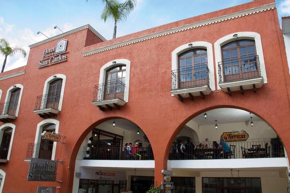 a red building with people sitting on the balconies of it at Hotel Plaza San Carlos in Xicotepec de Juárez