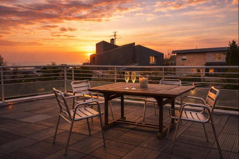 a wooden table and chairs on a deck with the sunset at le Sunset Loft 88 maison neuve et moderne in Sainte-Adresse