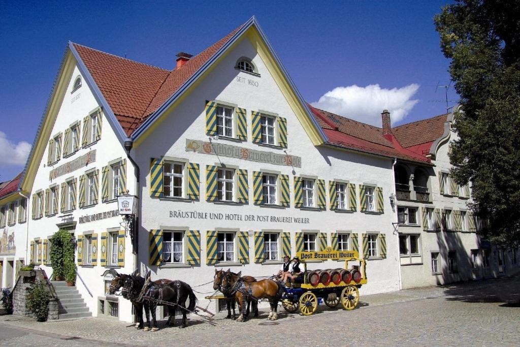 eine Gruppe von Pferden, die vor einem Gebäude einen Wagen ziehen in der Unterkunft Braustüble und Hotel zur Post in Weiler-Simmerberg