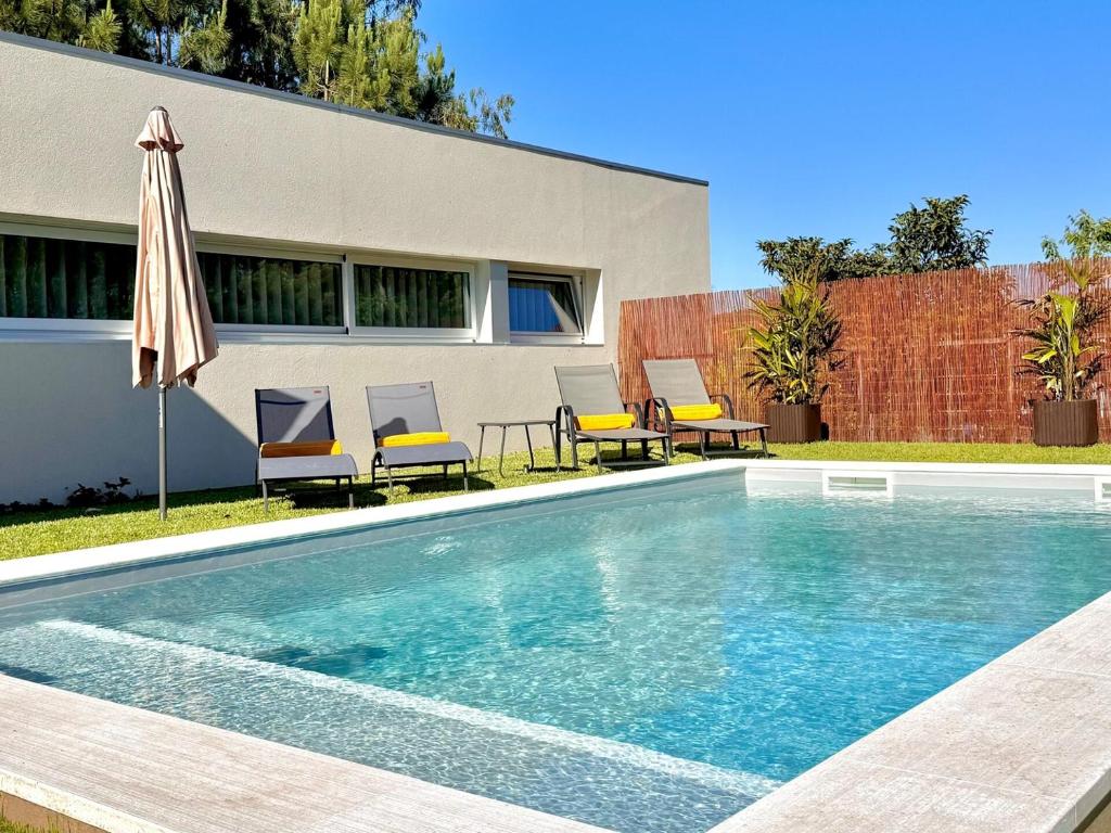 a swimming pool with chairs and an umbrella next to a house at Villa Branco - Private Pool & Garden in Barcelos