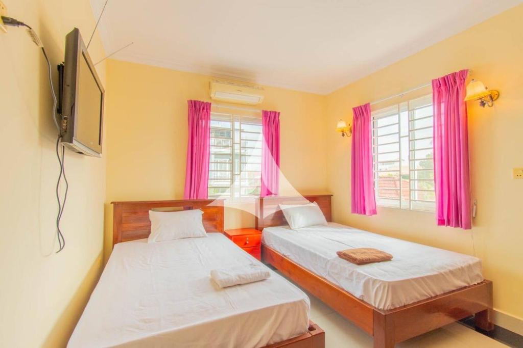 two beds in a small room with pink curtains at Serey Sok San Apartment in Phumi Ta Phul