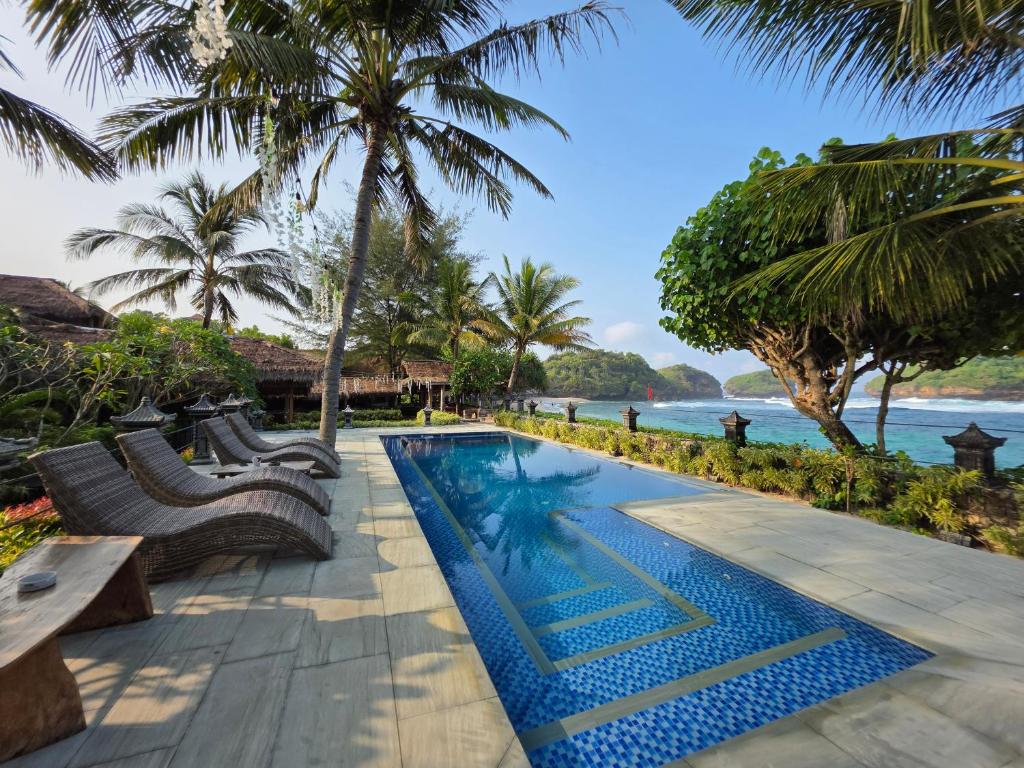 a pool with benches and the ocean in the background at Istana Ombak Eco Resort in Pacitan