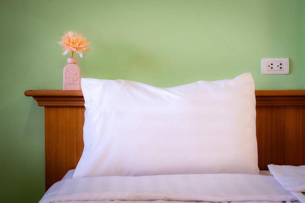 a bed with a white pillow and a vase with a flower at Saksiri apartment in Ban Si Than